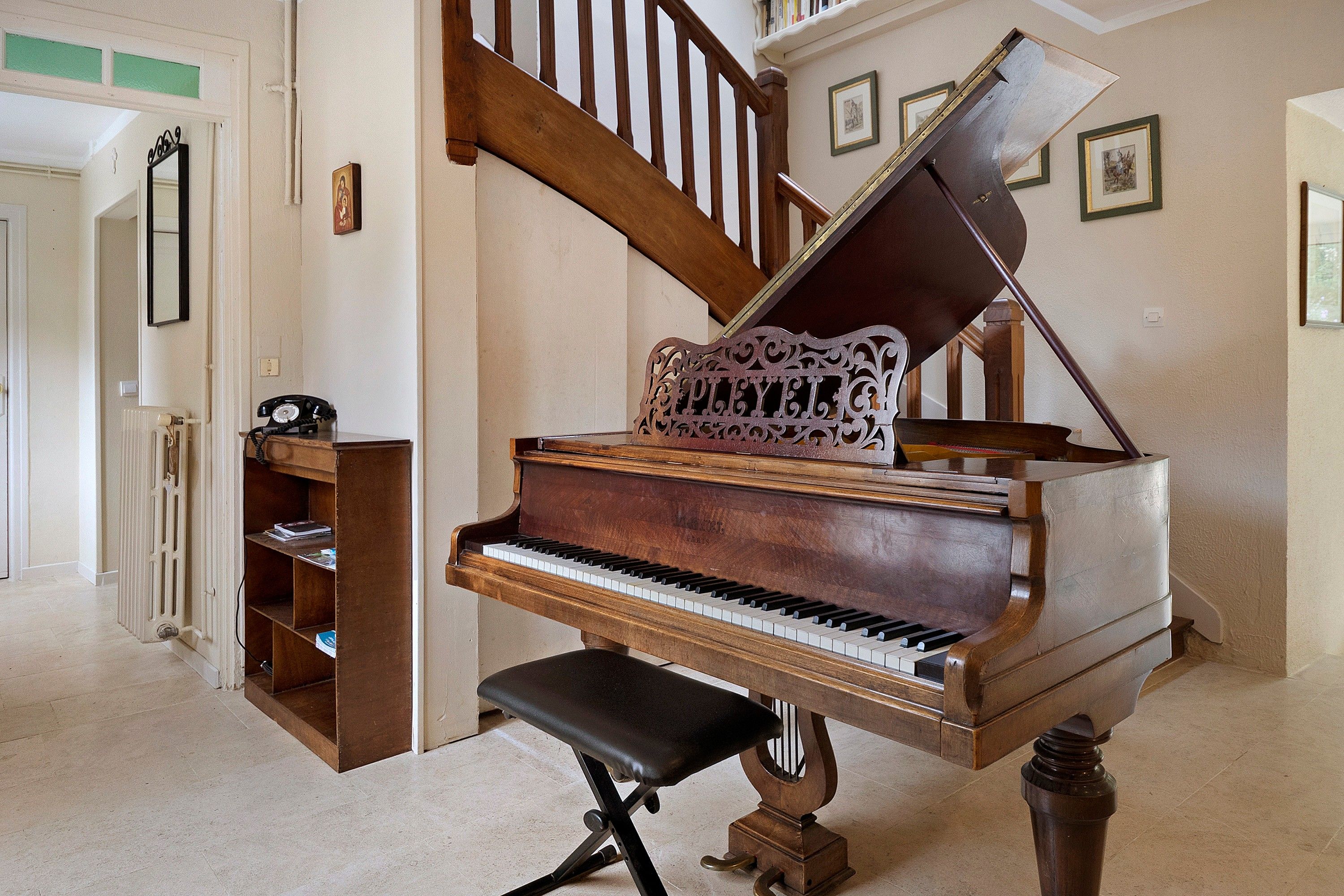 Un piano de cua en una habitació àmplia amb una escala de fusta i una prestatgeria.