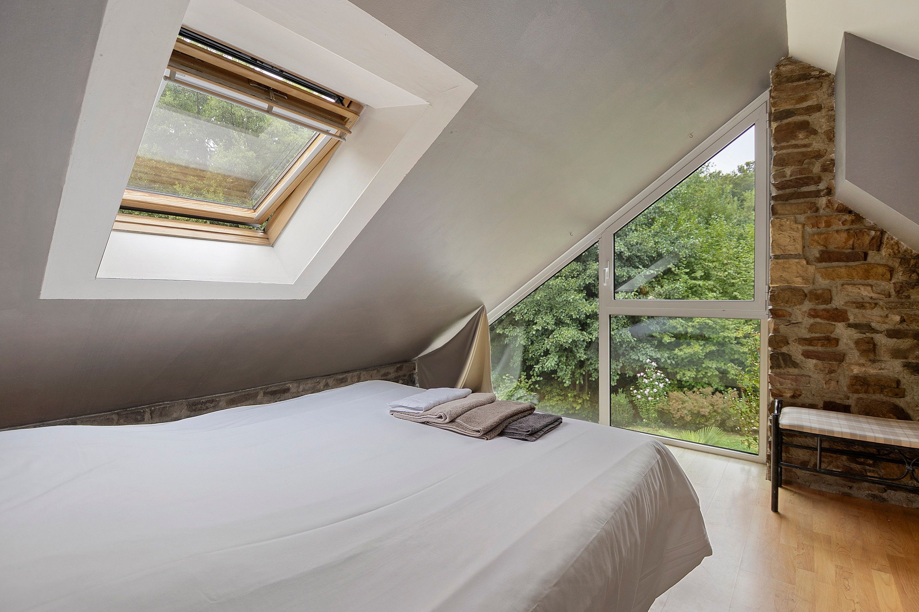 Ein Schlafzimmer mit Oberlicht, großem Fenster, Bett und Steinwand.