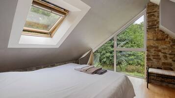 Ein Schlafzimmer mit Oberlicht, großem Fenster, Bett und Steinwand.