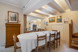 A dining room with a long table, wooden chairs, and a white tablecloth. There are framed pictures on the walls, a stone wall, and a wooden cabinet with a mirror. - Holiday Home 'Le Petit Moulin Du Pré Saint-Gorgon' with Private Terrace, Private Garden and Wi-Fi (Feuguerolles-Bully)