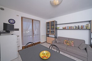 Una sala de estar con sofá, mesa de comedor, estantería y televisor.