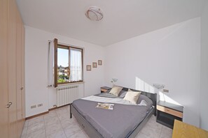 Un dormitorio con cama, mesitas de noche, ventana y radiador.