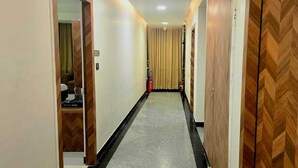 A hotel corridor with wooden doors, a fire extinguisher, and a carpeted floor. - Hotel Kutumb Vatika (Haldwani)