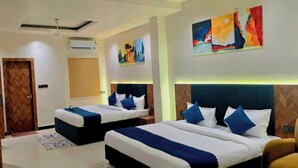 A hotel room with two beds, a wooden wardrobe, a desk with a chair, and artwork on the walls. - Hotel Kutumb Vatika (Haldwani)