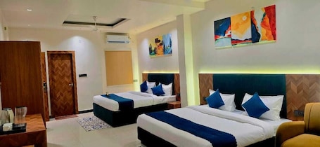 A hotel room with two beds, a wooden door, a wall-mounted air conditioner, and abstract wall art.. Hotel Kutumb Vatika