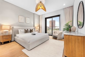 Ein modernes Schlafzimmer mit einem großen Bett, Nachttischlampen, einem runden Holztischchen, Blick auf die Stadt durch ein großes Fenster und einer Deckenleuchte.