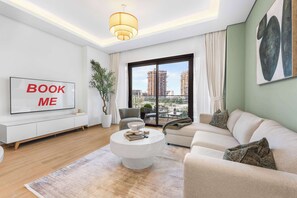 Ein modernes Wohnzimmer mit einer Couch, einem Couchtisch, einem Fernseher und einem großen Fenster mit Blick auf Gebäude.