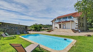 A swimming pool with lounge chairs, a two-story house with a balcony, and a stone wall in the background. - Casa de São Silvestre: Mountain View, Private Pool & Wi-Fi in Venade (Ferreira)