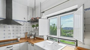 A kitchen with a large window, white cabinets, and a stainless steel range hood. - Casa de São Silvestre: Mountain View, Private Pool & Wi-Fi in Venade (Ferreira)