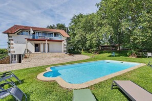 A two-story house with a swimming pool, a balcony, and a well-maintained lawn.