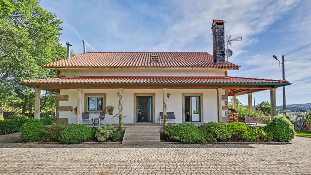 A two-story house with a tiled roof, a chimney, and a covered porch with outdoor seating. - Casa de São Silvestre: Mountain View, Private Pool & Wi-Fi in Venade (Ferreira)