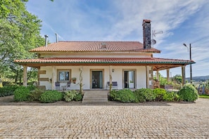 A two-story house with a tiled roof, a chimney, and a covered porch with outdoor seating.