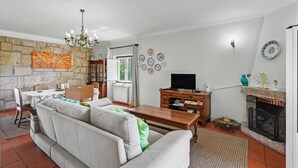 A living room with a sofa, a wooden coffee table, a television, a fireplace, and a stone wall. - Casa de São Silvestre: Mountain View, Private Pool & Wi-Fi in Venade (Ferreira)