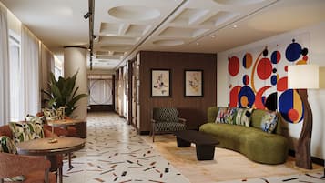 A modern hotel lobby with a checkered armchair, a green sofa, a round table, and a patterned floor.