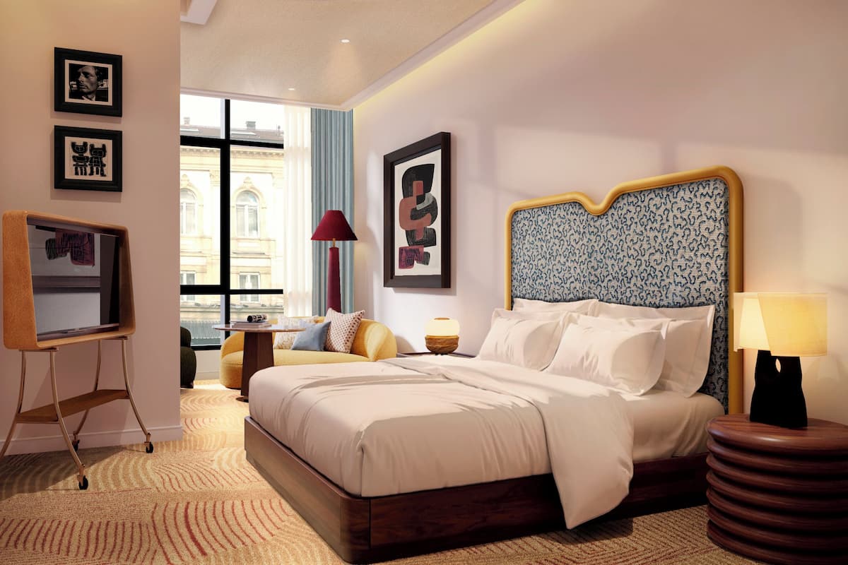 Una habitació d'hotel moderna amb un llit gran, escriptori, cadira, làmpada i obres d'art a les parets.
