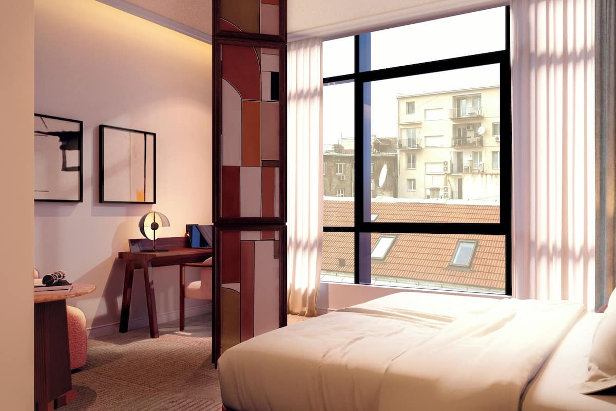 Una habitació d'hotel amb una finestra gran, una taula de treball, una cadira, un llit i una làmpada.