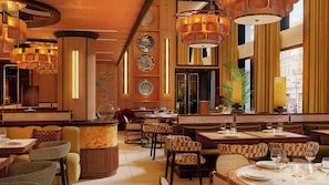 Een restaurant met verschillende eetgedeeltes, waaronder hoekbankjes en tafels, een warm interieur en grote ramen.