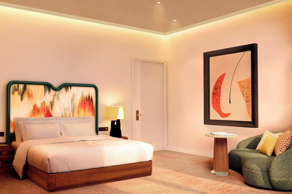 Habitació d'hotel moderna amb llit, taulell de nit, làmpada, obra d'art i una poltrona verda.