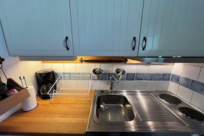 Eine Küche mit hellblauen Schränken, einer Edelstahlspüle, einer Kaffeemaschine und einem Wasserkocher.