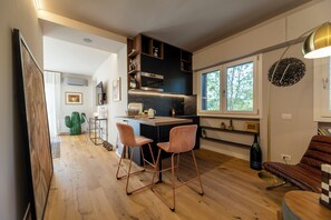 A modern kitchen with wooden flooring, a bar area with two stools, and a large window providing natural light. - Casa Mommi - Romantic Retreat in the Green Heart of Perugia (Perugia)
