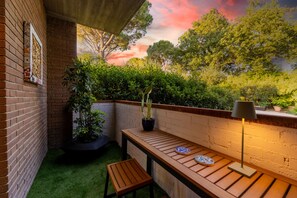 A wooden bench, a table, and a potted plant in a corner with a brick wall and a view of trees. - Casa Mommi - Romantic Retreat in the Green Heart of Perugia (Perugia)