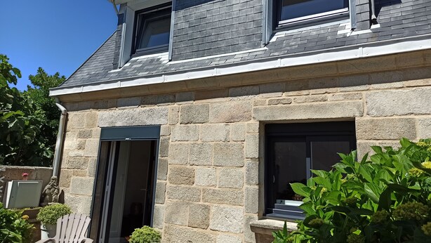 Une maison en pierre avec un toit à pignon, deux fenêtres et une porte.