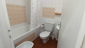 Une salle de bain équipée d’une baignoire, de toilettes, d’un bidet et d’un rideau de douche.