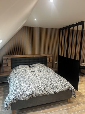 Een moderne slaapkamer met een groot bed, schuine plafond en verticale houten lambrisering.