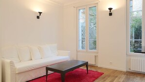 Ein Zimmer mit einem weißen Sofa, einem dunklen Holztisch, einem roten Teppich und zwei Wandleuchten.