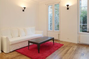 A room with a white sofa, a dark wooden coffee table, a red rug, and two wall-mounted lights. - Very nice 2-bed flat with a private garden in the 16th. Perfect for families (Paris)