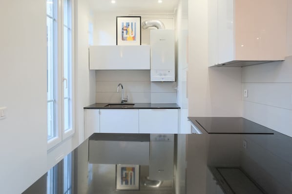 A modern kitchen with white cabinets, a black countertop, a stainless steel sink, and a built-in oven. - Very nice 2-bed flat with a private garden in the 16th. Perfect for families (Paris)