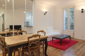 A modern living room with a dining area, white walls, and a large mirror. - Very nice 2-bed flat with a private garden in the 16th. Perfect for families (Paris)