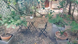 Ein von einer Hecke umgebener Gartenbereich mit einem Holztisch und Stühlen, umgeben von Blumentöpfen und Bäumen.