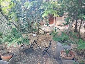 A fenced garden area with a wooden table and chairs, surrounded by potted plants and trees. - Very nice 2-bed flat with a private garden in the 16th. Perfect for families (Paris)