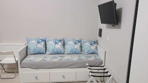 Ein kleiner, moderner Raum mit einem weißen Sofa, einem Wand-Fernseher, einem kleinen Tisch und einem Sessel.