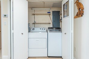 A laundry room with two washing machines, a blue door, and a wooden bird decoration. - Beautifully Renovated 2 Bedroom Ocean Front Condo! Fountainhead Towers 1201 (Ocean City)