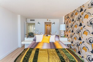 A bedroom with a bed, bedside tables, a mirror, a wall with a patterned wallpaper, and a door leading to another room. - Beautifully Renovated 2 Bedroom Ocean Front Condo! Fountainhead Towers 1201 (Ocean City)