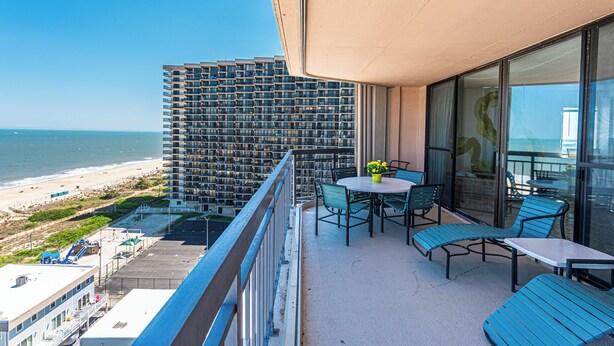 Un balcone con vista sulla spiaggia e sull'oceano, arredato con sedie e un tavolo.