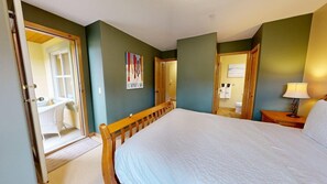 Ein Schlafzimmer mit einem Bett, einer Tür zu einem Badezimmer und einem kleinen Tisch mit einer Lampe.