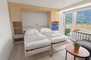 A room with two beds, a TV, a balcony with a view, and a small table with a plant. - Bright apartment with superb terrace and view (Leukerbad)