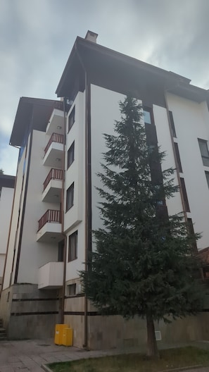 A multi-story building with balconies, a tree in front, and a yellow storage unit. - Borovets Apartments, Flora Violet Residence (Samokov)