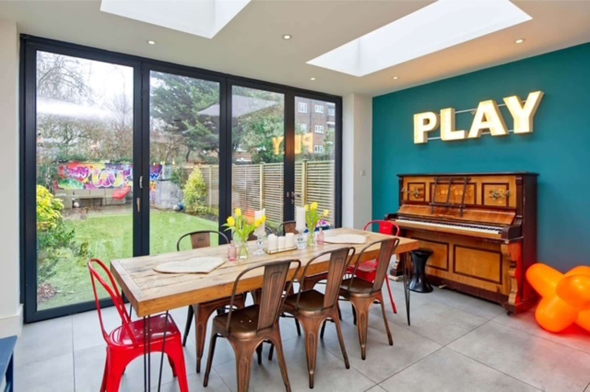 A dining area with a piano, a table with chairs, and a large window with a view of a garden.