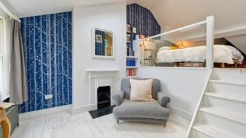 A bedroom with a bunk bed, a fireplace, a chair, and a bookshelf.