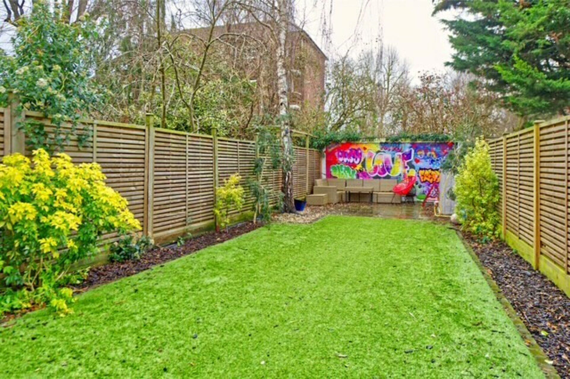 A well-maintained backyard with a grassy lawn, a wooden fence, and a colorful graffiti wall.