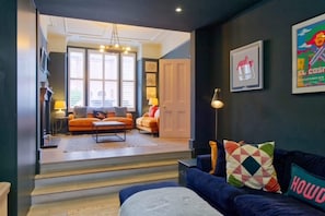 Ein modernes Wohnzimmer mit einer Couch, einem Couchtisch und einer Lampe. Eine Treppe führt in einen anderen Raum.
