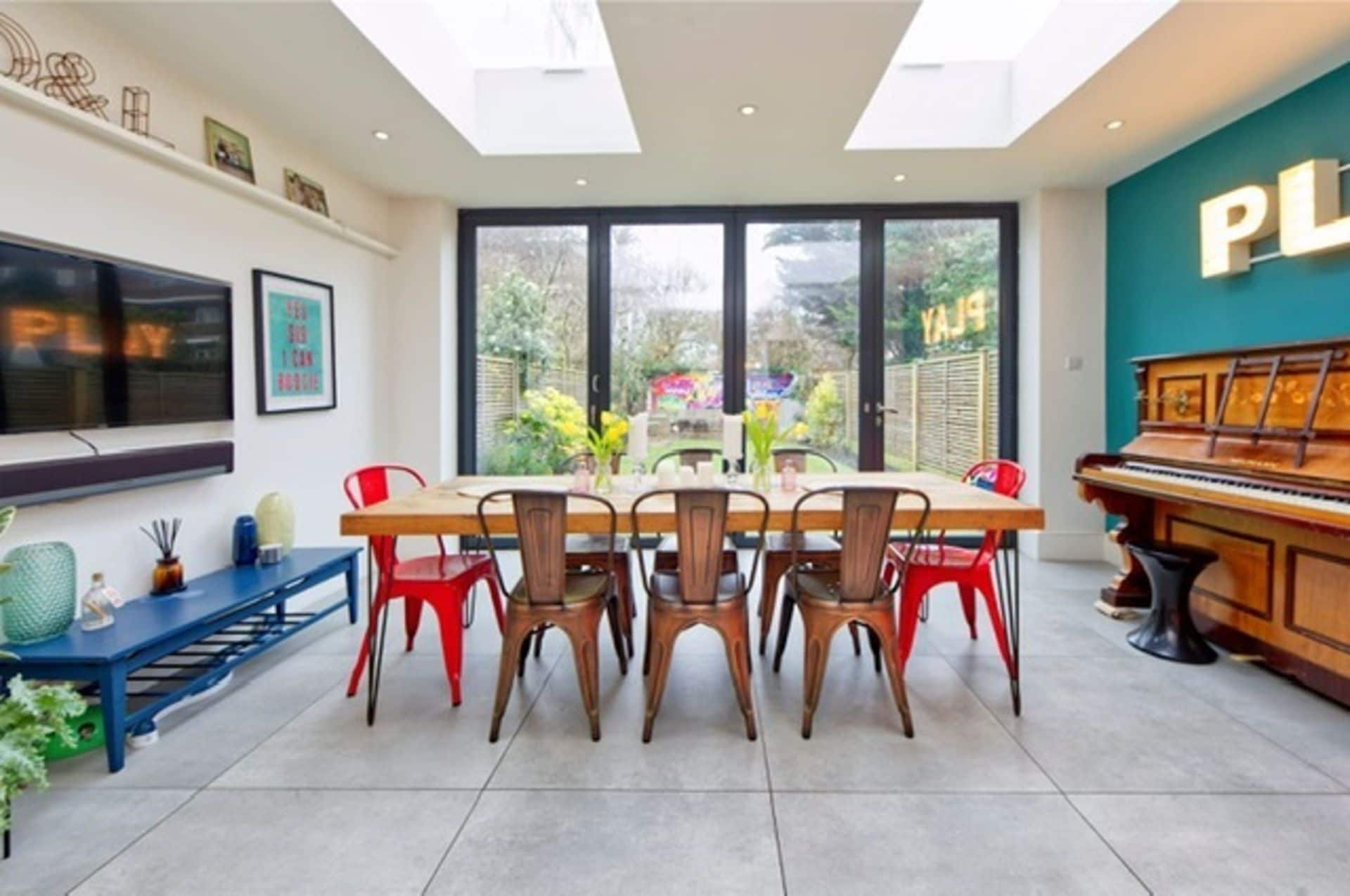 A dining area with a large table, multiple chairs, a piano, and a TV on the wall.