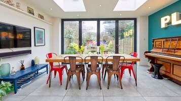 A dining area with a large table, multiple chairs, a piano, and a TV on the wall.