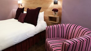 Une chambre d’hôtel avec un lit, des oreillers, une table de chevet ornée d’un vase de fleurs et un fauteuil à rayures.