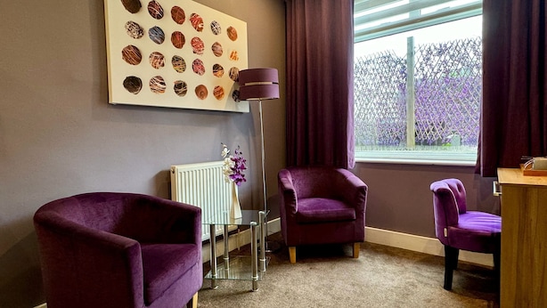 Une pièce avec deux fauteuils violets, un radiateur blanc, un lampadaire et une fenêtre ornée de rideaux violets.