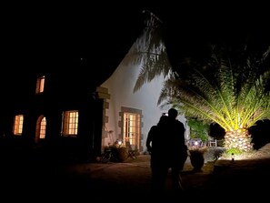 A house with a large tree in front, a person standing, and a lit-up area. - Charming property, family home, panoramic ocean view, large, quiet garden (Plouarzel)